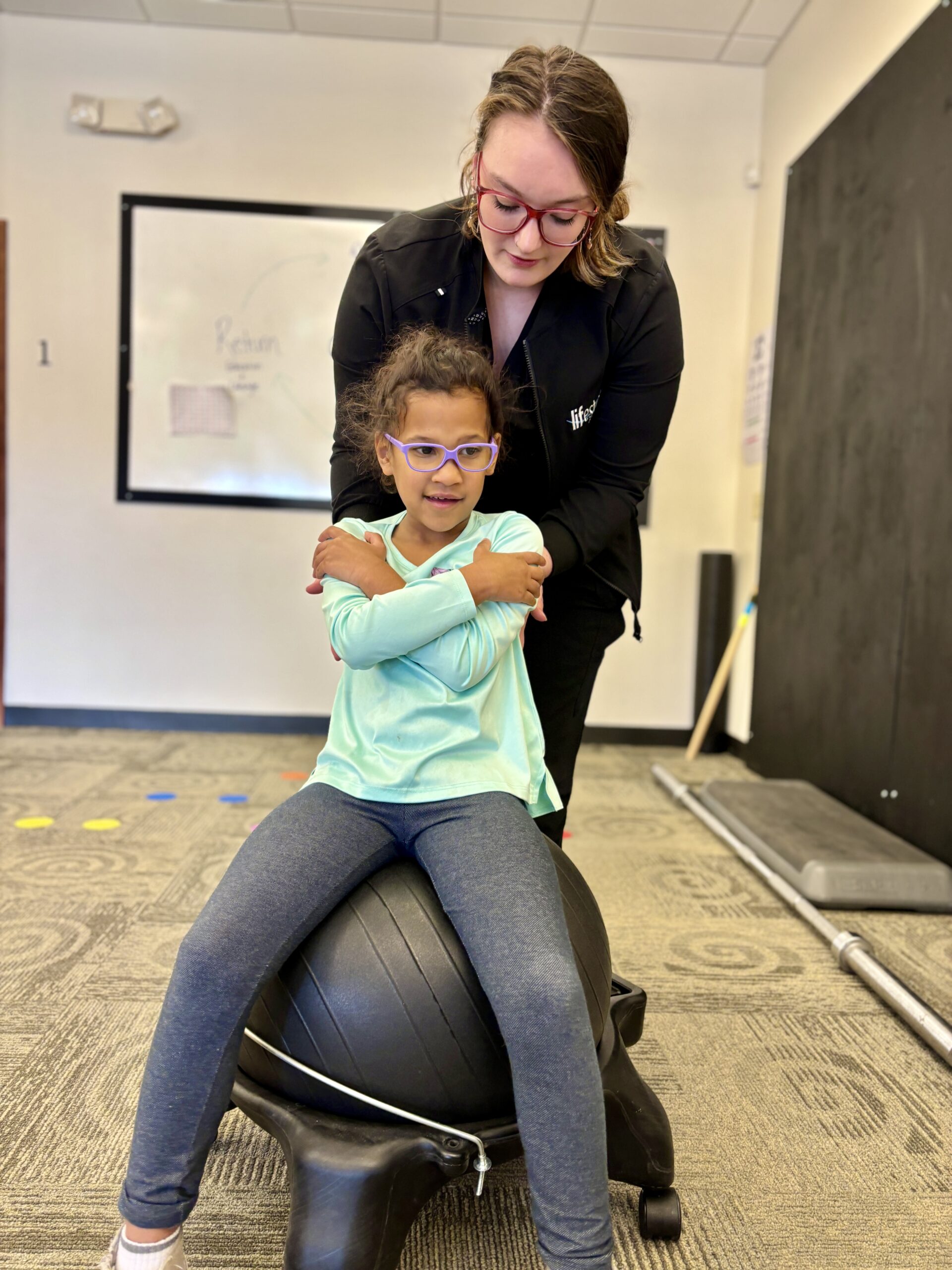 Little girl sitting on an exercise ball balancing with help from a provider